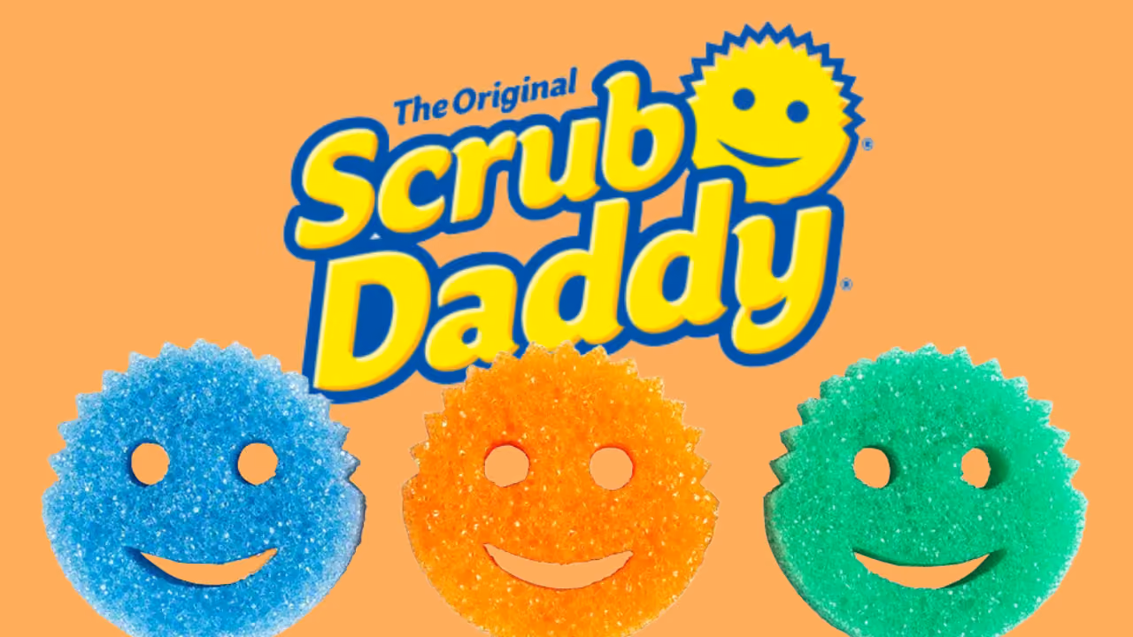 Three smiling Scrub Daddy sponges — blue, orange and green — beneath The Original Scrub Daddy logo on orange