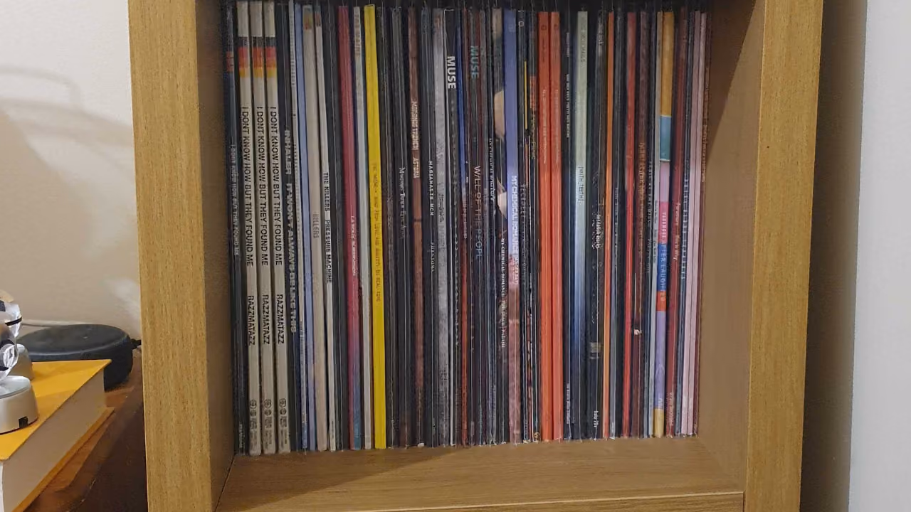 A record shelf packed with vinyl seen spine-on, among them Razzmatazz by I Don't Know How But They Found Me, The Killers, Muse and My Chemical Romance