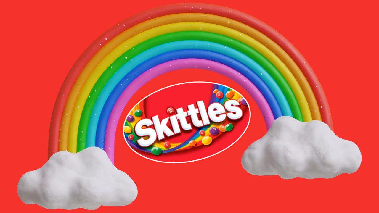 The Skittles logo under a claymation rainbow arcing between two white clouds, on red