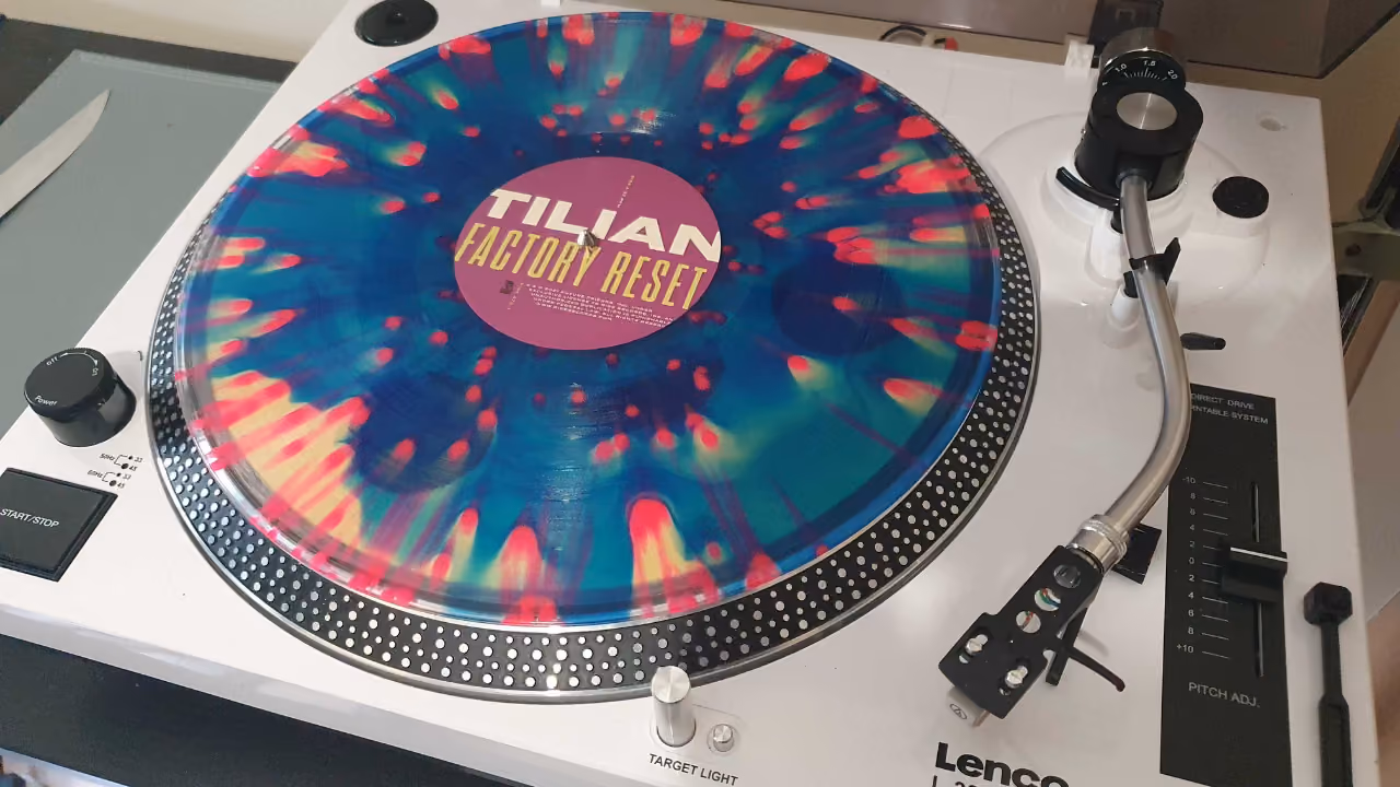 A splatter-coloured vinyl record — blue, yellow and red — turning on a white Lenco turntable, its label reading Tilian, Factory Reset