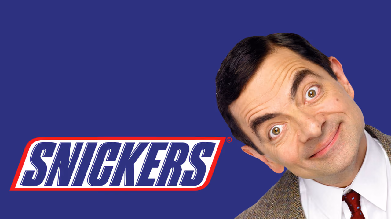 Rowan Atkinson as Mr Bean, head tilted and eyebrows raised, beside the Snickers logo on deep blue