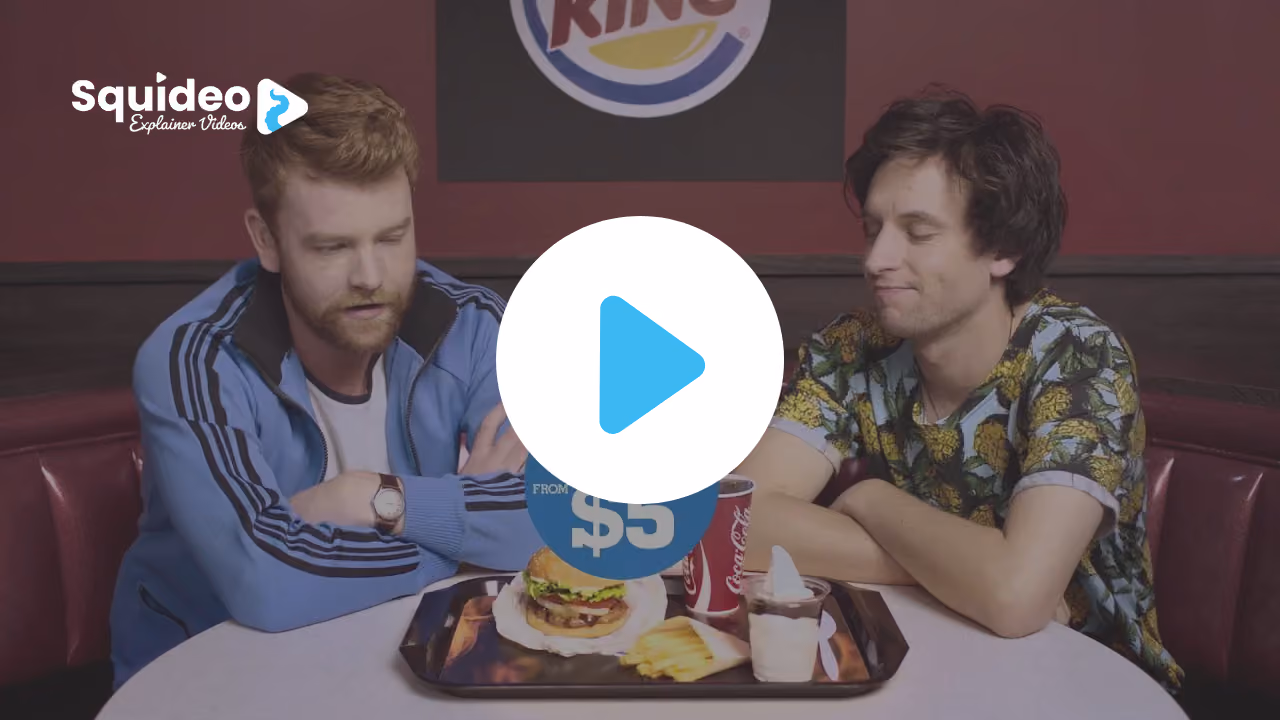 Two men in a Burger King booth looking down at a tray with a burger, fries, a Coca-Cola and a sundae, marked from $5