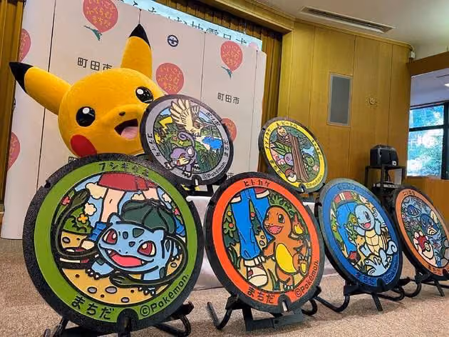 Six painted Pokémon manhole covers on display stands, Bulbasaur, Charmander, Squirtle and others among them, with a Pikachu mascot standing behind