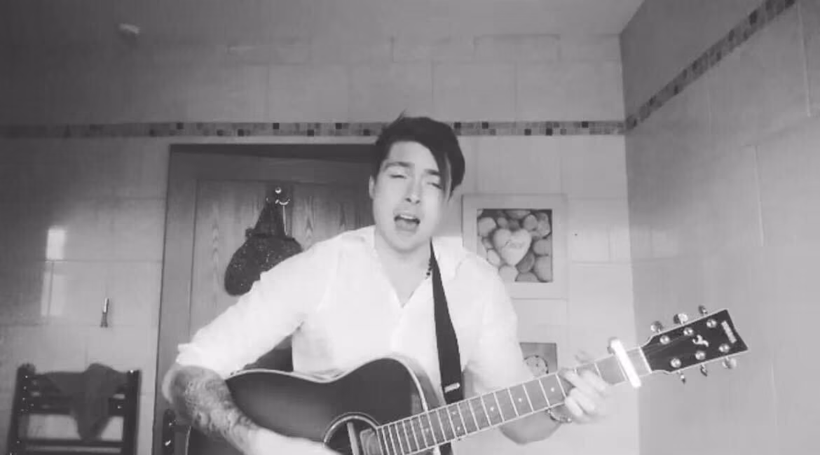 Black and white: a man in a white shirt singing and playing an acoustic guitar in a tiled kitchen