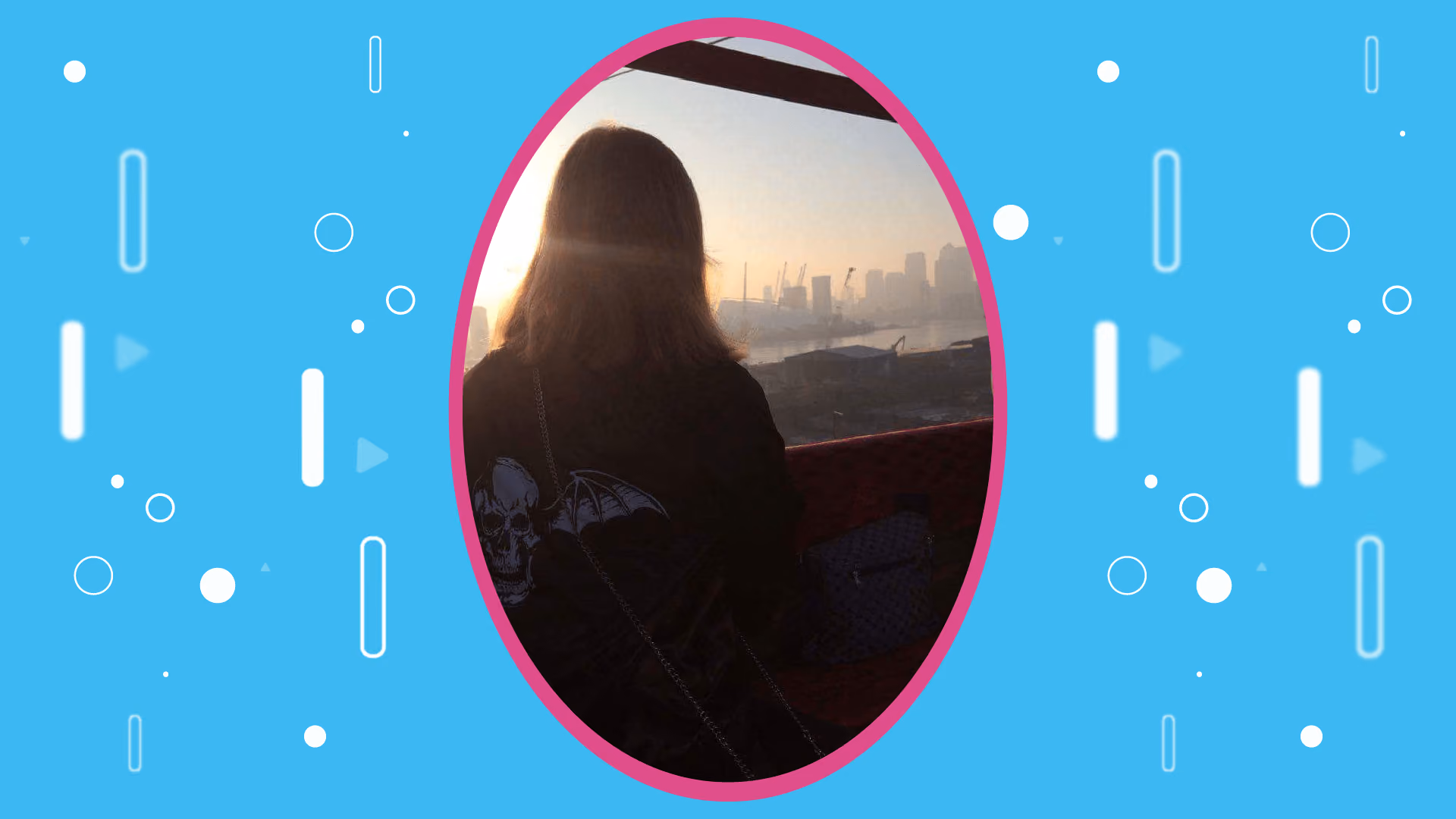 Seen from behind, a woman in an Avenged Sevenfold hoodie looking out over the Thames towards the O2 and the Canary Wharf skyline at sunrise