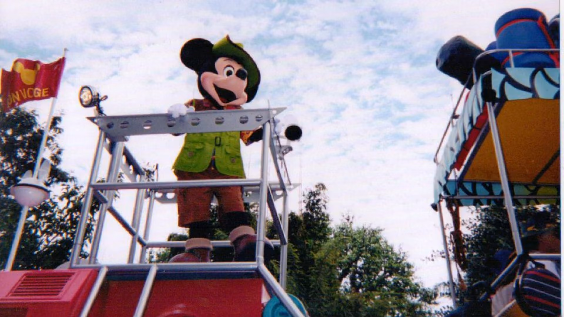 Mickey Mouse in a safari hat and green explorer's waistcoat riding a parade float, a Bon Voyage flag flying beside him