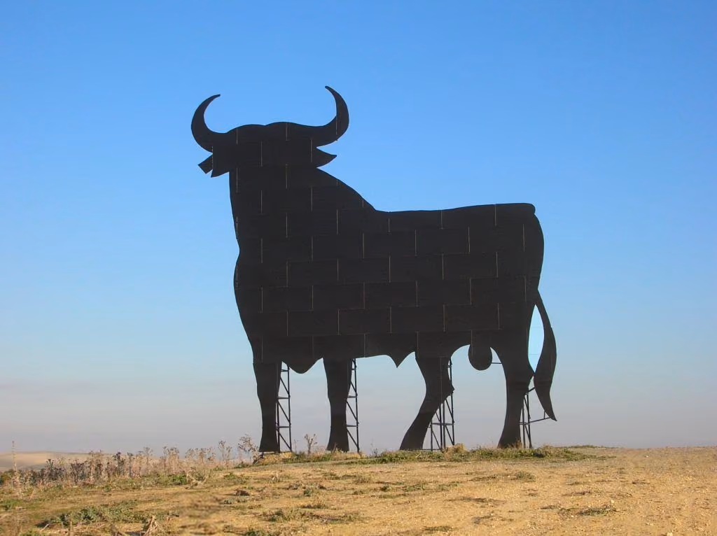 The Osborne bull — a huge black sheet-metal silhouette on scaffolding — standing on a bare Spanish hilltop against a clear sky