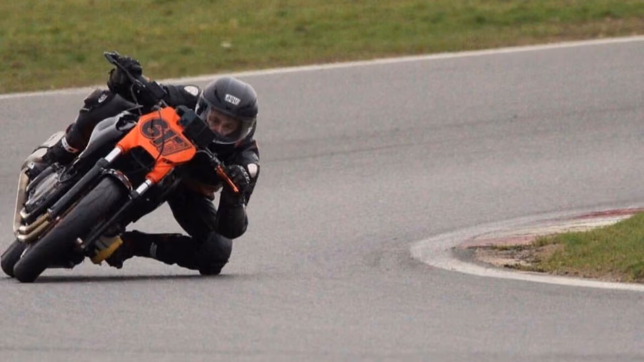 A motorcyclist leaning hard into a bend on a race circuit, knee down, on an orange and black bike