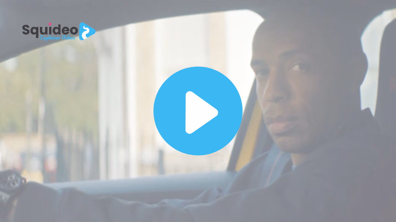 A footballer at the wheel of a car, looking to camera, city street blurred behind him