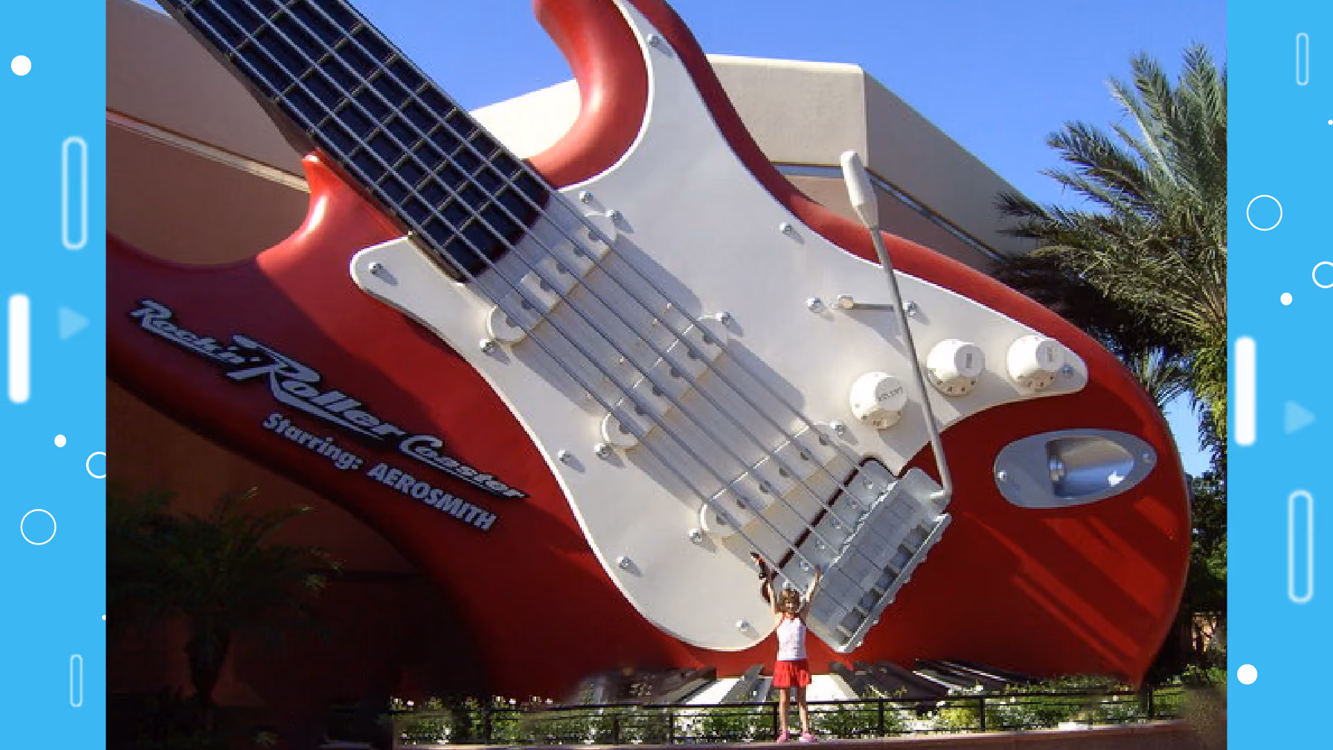 A child standing with both arms raised in front of the giant red Fender Stratocaster outside Rock 'n' Roller Coaster Starring Aerosmith