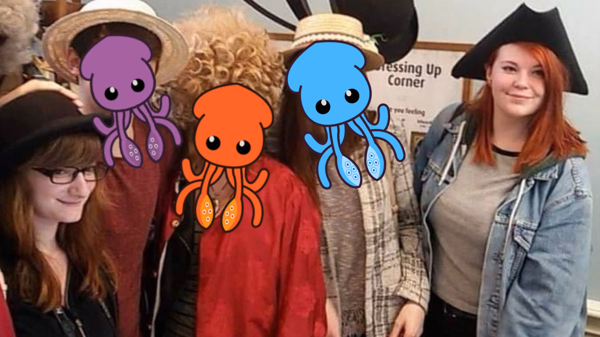 Five people in a dressing-up corner in hats and wigs, three of their faces covered by purple, orange and blue cartoon squid