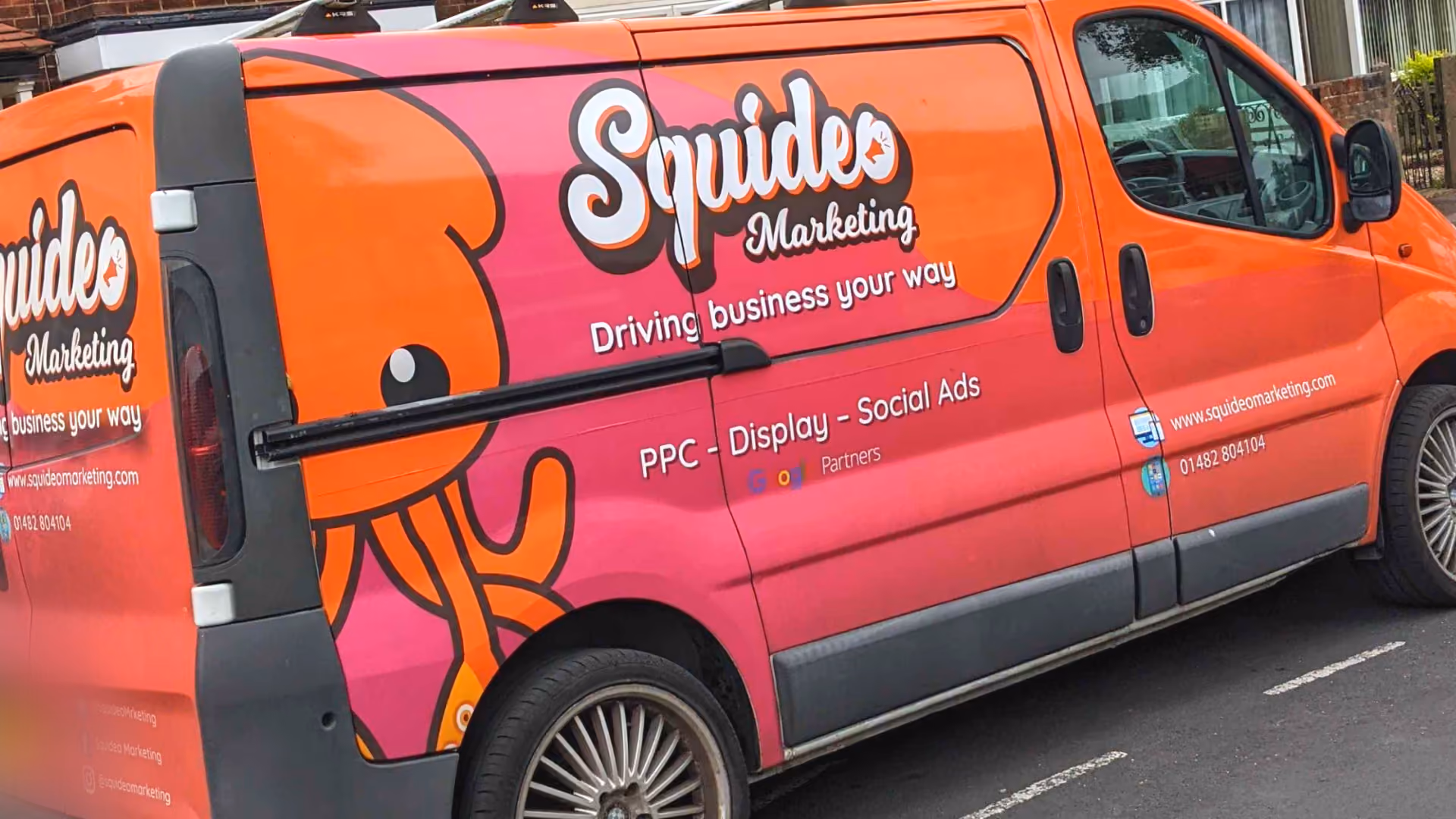 An orange and pink Squideo Marketing van, signwritten with a large squid character and the lines 'Driving business your way', 'PPC – Display – Social Ads', 'Google Partners', www.squideomarketing.com and 01482 804104
